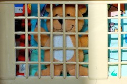 A teddy bear is smiling even though it is trapped behind bars