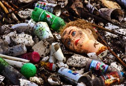 A doll's head lies among toys and beer cans on a garbage heap.